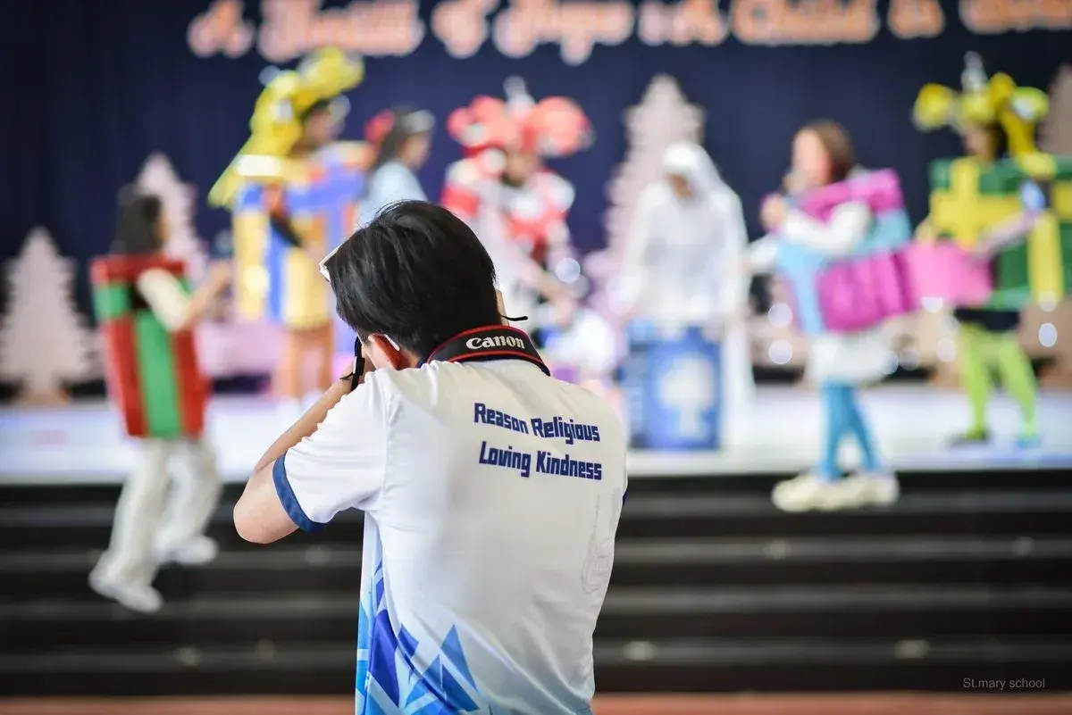 นักเรียนเซนต์เมรี่สวมเสื้อสกรีนคำว่า Reason Religious Loving Kindness ขณะบันทึกภาพการแสดงบนเวที